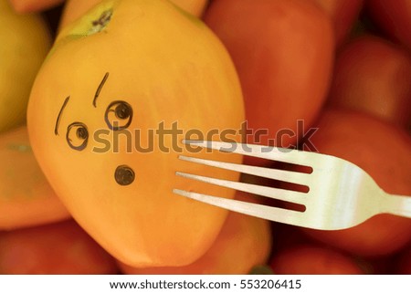 Steel fork near a orange tomato with an scared face, background