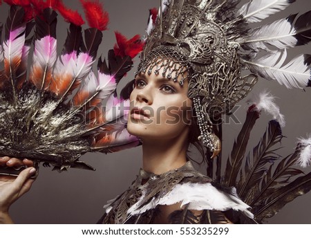 Portrait of woman in creative bronze crown and wearing, holding fan made of feathers Royalty-Free Stock Photo #553235299