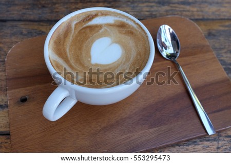 Hot white coffee cup with heart shape latte art on wooden table 