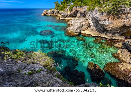Beautiful clear turquoise water near rocks and cliffs in Negril Jamaica. Caribbean paradise island and water at the seaside with a blue sky and nice day light Royalty-Free Stock Photo #553342135