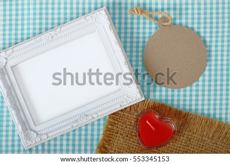 Top view of empty white photo frame and paper tag next red heart sign from candle in glass over the fabric, clipping path ready to put photographs.