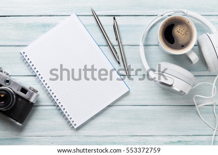 Headphones, notepad, camera and coffee cup on wooden table. Top view with copy space