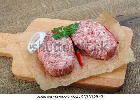 Raw burget cutlet with onion and parsley on wood background