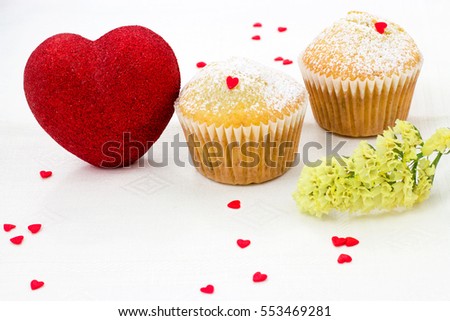Two muffin in paper molds, shiny red heart, yellow flower and a lot of
small sugar hearts on a white background. Valentine's Day breakfast. Space for copy