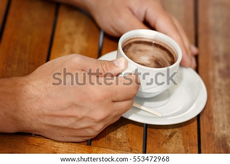Man hands holding cup of coffee at cafe outdoors summer. Male drink cappuccino in restaurant closeup. Coffee time and breakfast. Man with mug of hot chocolate enjoying life in cafe.