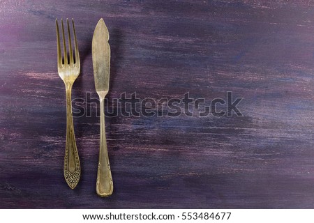An overhead photo of a vintage fork and a knife on a purple wooden background texture. A restaurant menu or special offer banner design template