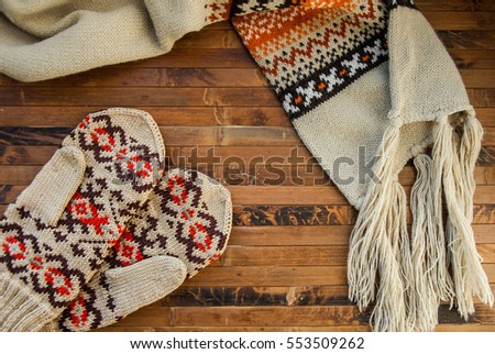 Winter warm scarf and mittens with christmas pattern on a wooden background. Cozy warm clothing. Royalty-Free Stock Photo #553509262
