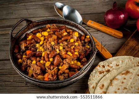 Traditional Mexican and Chilean dish of chilli con carne. In the rustic pan, next to tortillas and fresh vegetables on a wooden table, copy space