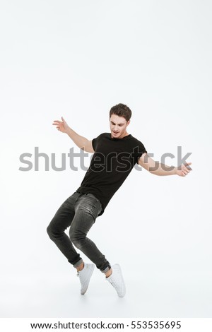 Picture of attractive young man dressed in black t-shirt dancing over white background looking down.