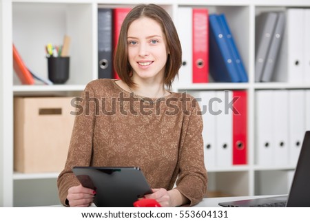 Smiling brunette woman holding a tablet in his hands, looking into the camera.