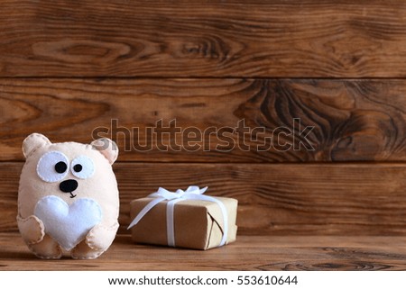 Cute felt bear toy holds heart, handmade gift box in craft paper on brown wooden background with empty place for text. Valentine's day, mother's day or birthday background 