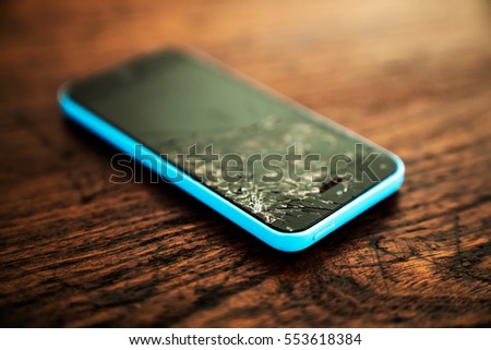 Mobile smartphone with broken screen on wooden background.