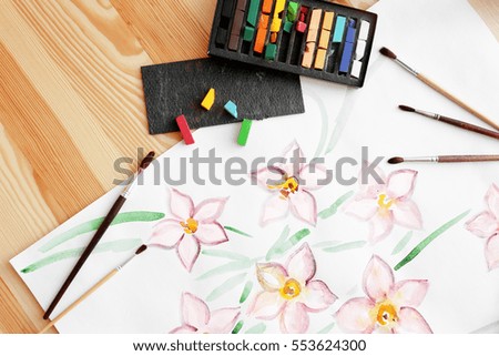 Crayons, brushes and beautiful picture on wooden table