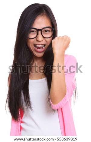 Studio shot of young happy Asian teenage girl smiling and looking motivated isolated against white background