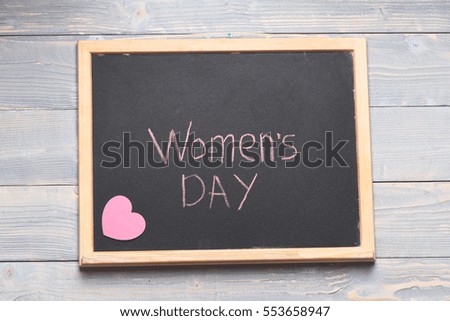 inscription Womens day painted by chalk with pink heart on black board on blue vintage wooden background, top view