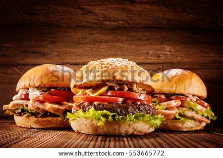 Low angle front view on three large chicken, beef and shrimp burgers stuffed with delicious toppings over wooden table