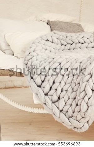 The bed suspended from the ceiling, an unusual bed. Grey big cozy blanket knit. Bed, Scandinavian style, gray plaid.