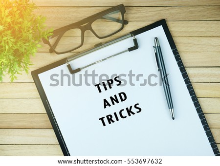 Top view of clipboard and white sheet written with TIPS AND TRICKS on wooden background. Business Concept. 