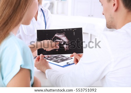 Gynecology consultation. Doctor showing ultrasound scan  of baby to couple