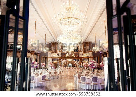 Look from afar at luxurious restaurant hall prepared for wedding dinner Royalty-Free Stock Photo #553758352