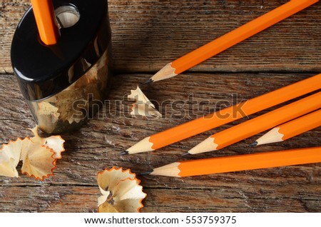 A top view image of several yellow wooden pencils with pencil shavings on an old desk top. 