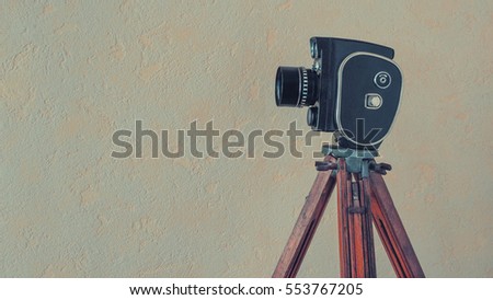 The old camera on a wooden tripod stands on a background of a wall