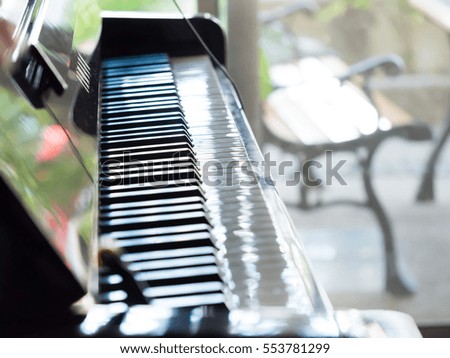 Closeup of piano in the room and blurry chair in the garden