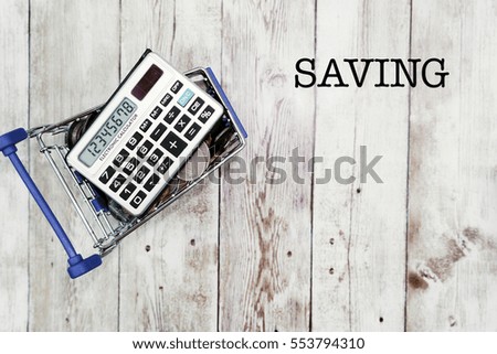 Coins and calculator on shopping chart with SAVING wording on wooden background. Financial, economy, taxing, saving concept