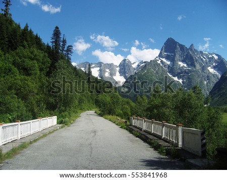 Snowy mountains and blue sky with clouds. Road in a Caucasus mountains.
