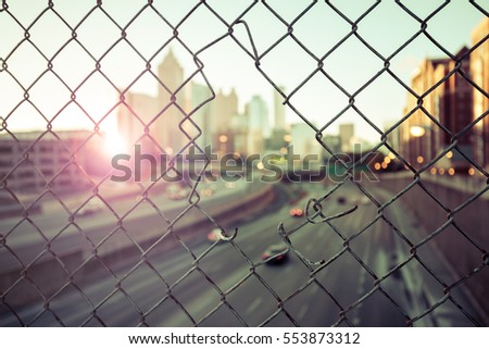 Morning city skyline through the wire mesh fence. Sunrise cityscape background