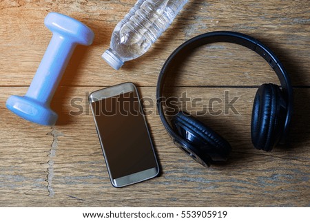 smart phone with headphones,blue dumbbell on wooden floor background, copy space