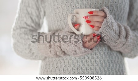 Woman wearing knitted sweater and gloves holding a cup of hot coffee, humorous home heating energy saving Royalty-Free Stock Photo #553908526