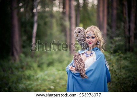 Girl in white dress and blue cloak with the owl on his shoulder, in the forest