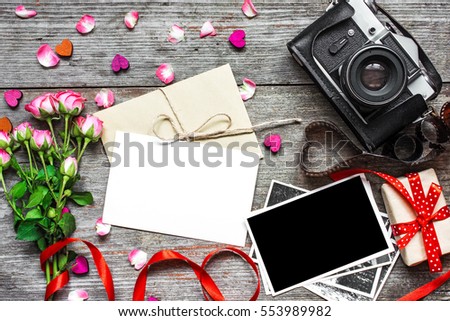 blank white greeting card with retro camera, blank photo, gift box and pink roses flower bouquet over wooden background. top view. valentines day background