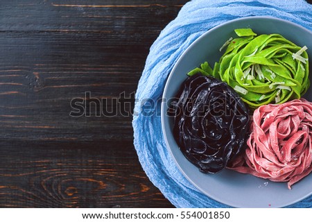 three delicious pasta. black paste, green pasta and pasta fuchsia. gray plate on a wooden background.