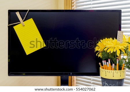 Large computer monitor with yellow reminder note clipped to left corner, pencils, ruler and flowers in decorative cup, space for text
