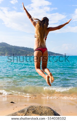young woman with long hair wearing bikini and happily jumping on dreamlike vacation on the beach 