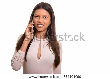 Studio shot of young happy Brazilian woman smiling while talking on mobile phone isolated against white background