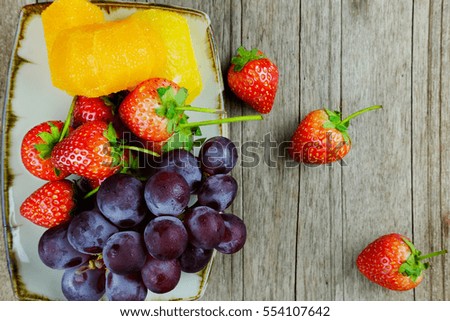 Healthy fruit with strawberries, orange and grape in plate concept on wood table background, top view and selective focus.