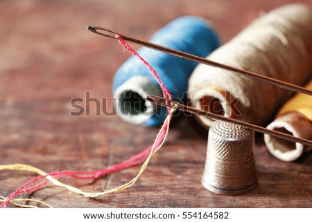 Thimble and needles near thread on old wooden background