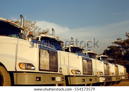 A line of heavy duty freight trucks parked in a row at a dirt road Royalty-Free Stock Photo #554173579