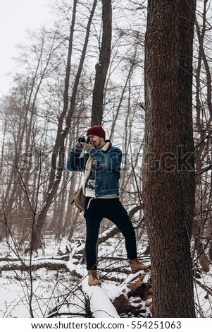 stylish hipster traveler holding camera and making photo in snowy forest. wanderlust and adventure concept with space for text. atmospheric moment