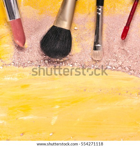 Makeup brushes and lipstick on a vibrant golden yellow background, with traces of powder and blush on it; a square template for a makeup artist's business card or flyer design; with copyspace