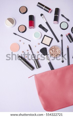 A pink leather make up bag, with cosmetic beauty products spilling out on to a pastel purple background