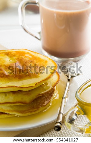 Glass mug with cocoa, silver spoon, honey and pancakes for dessert closeup with shallow depth of field.