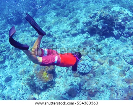 Snorkeling man dives to sea bottom. Young coral reef in deep blue water. Modern snorkeling gear - full-face mask, long fins, swimsuit. Snorkeler in tropical lagoon underwater photo. Active holiday