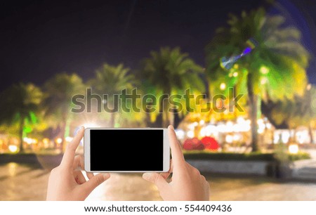 woman use mobile phone and blurred image of the park at night with a roll of big palm trees