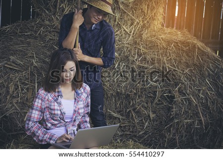 Young farming couple with laptop computer in the barn against hay background.
