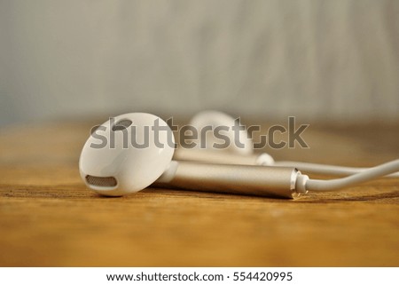 Macro detail of white modern earphones in futuristic design on the wooden background as a symbol of listening to music with the trendy equipment