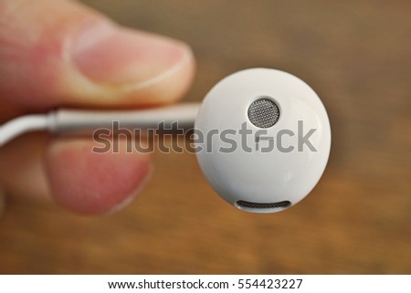 Male hand holding white modern earphone in futuristic design above the wooden background as a symbol of listening to music with the trendy equipment